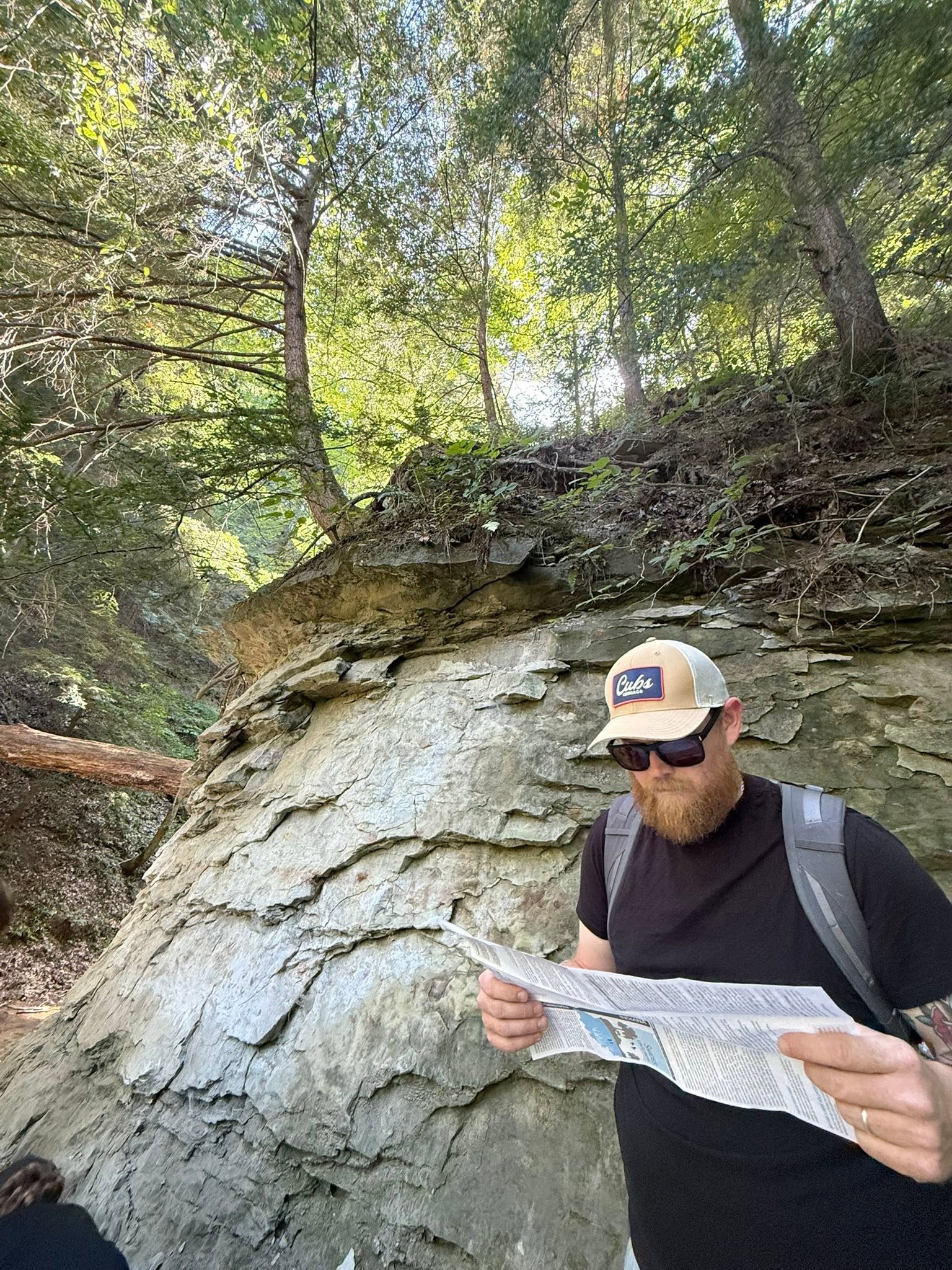 Seth Beaty reading beside a rock face on a wooded trail